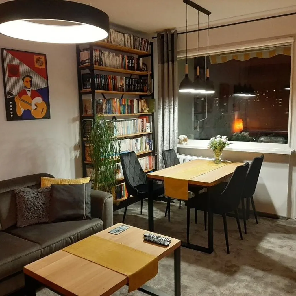 Regał metalowy czarny z drewnianymi półkami, elegancki loftowy, z litego drewna dębowego, stolik kawowy na metalowych nogach z litego dębu stojący koło kanapy, oraz duży stół z litego dębu obiadowy na metalowych nogach i cztery krzesła
