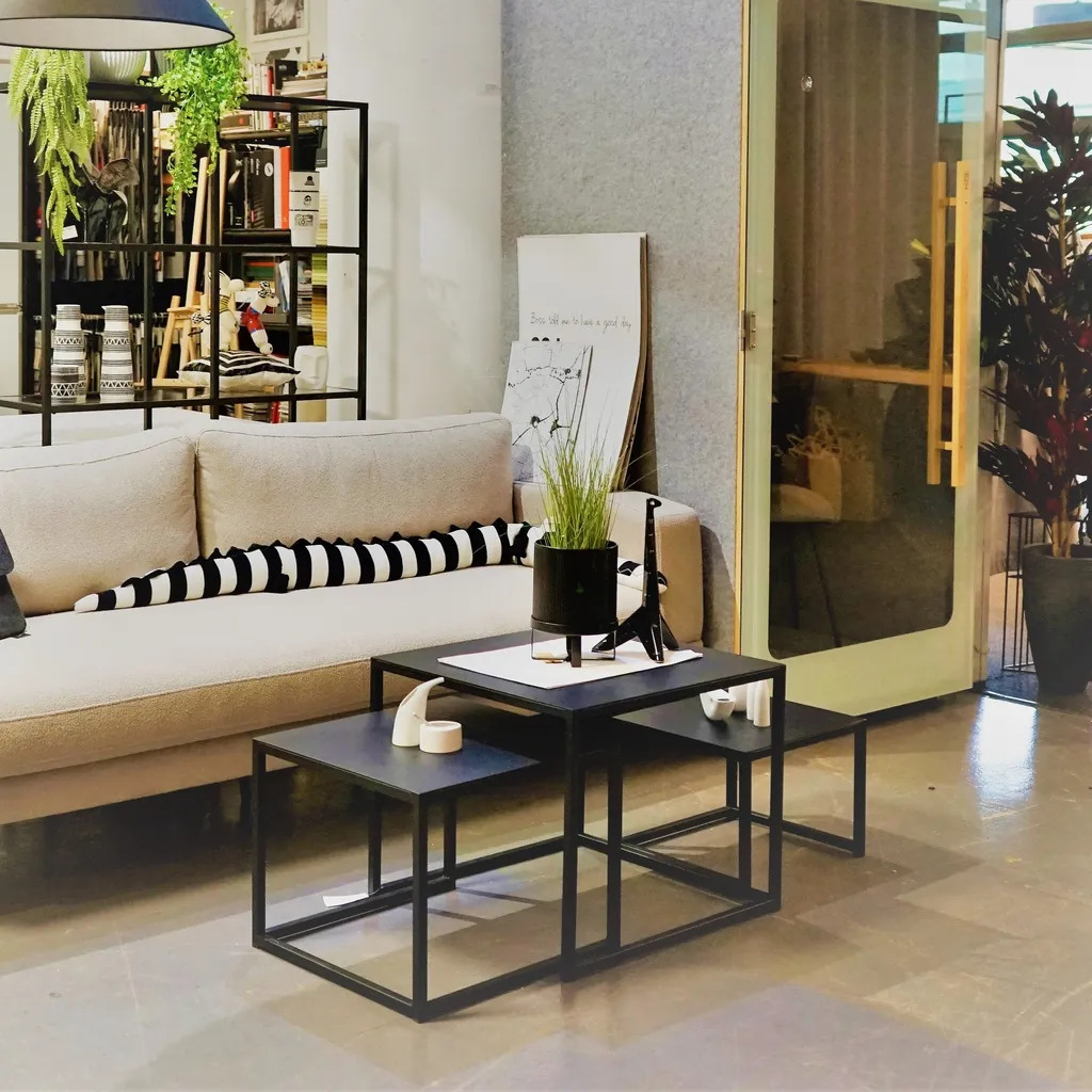 Nowoczesny salon z beżową sofą z pasiastymi poduszkami, zestawem czarnych metalowych stolików kawowych, rośliną doniczkową i lampą.
